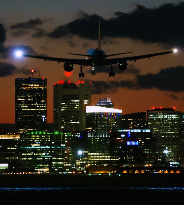 Plane landing over the Boston skyline at dusk